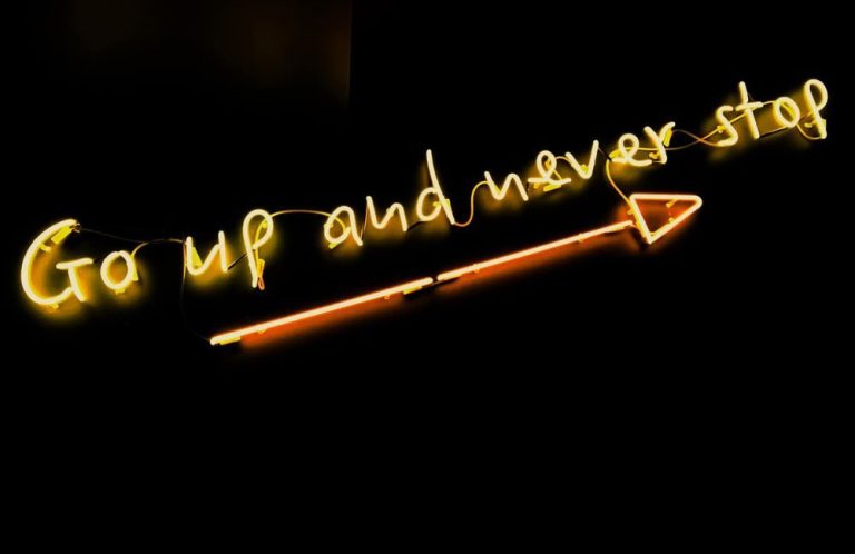 Neonbeschriftung: „Go up and never stop“ mit Pfeil nach oben.